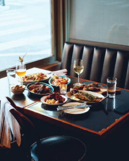 Spread of dishes and wine on a booth table beside a window in a New Orleans restaurant Evviva